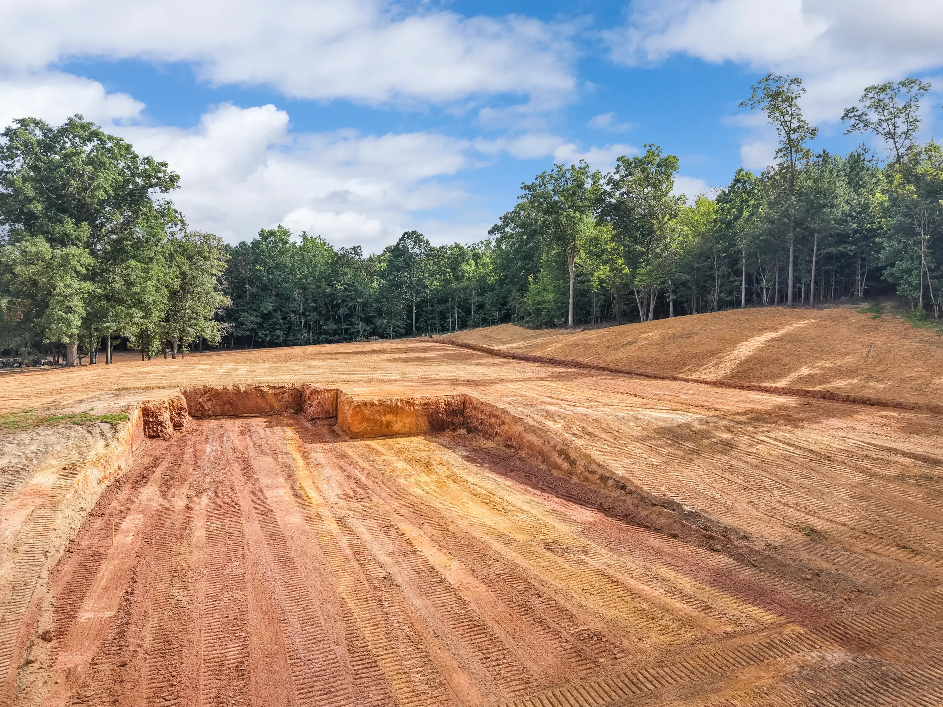 Excavated site with graded earth, cut basin, and machine-tracked soil work