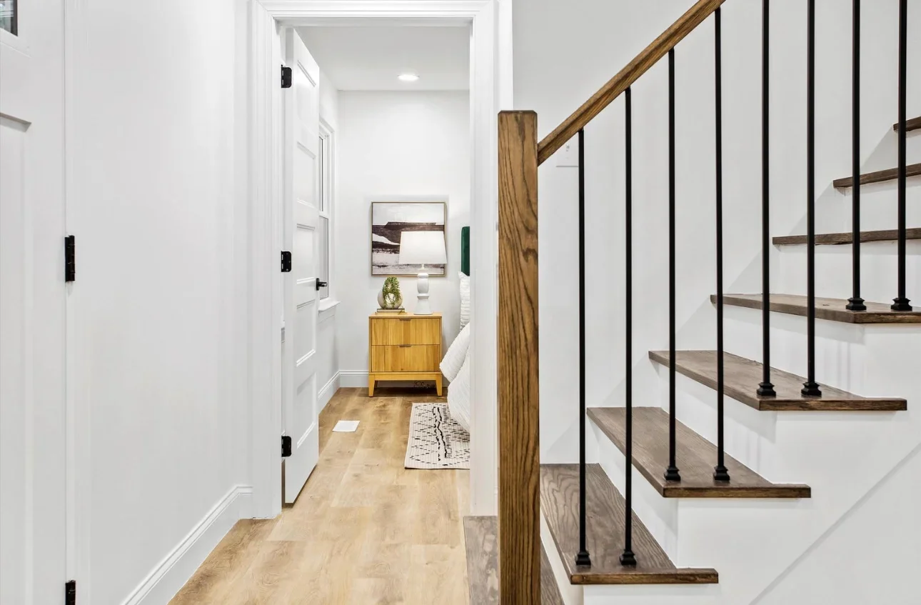 Modern staircase with wood treads, black metal railings, and white painted walls in renovated hallway