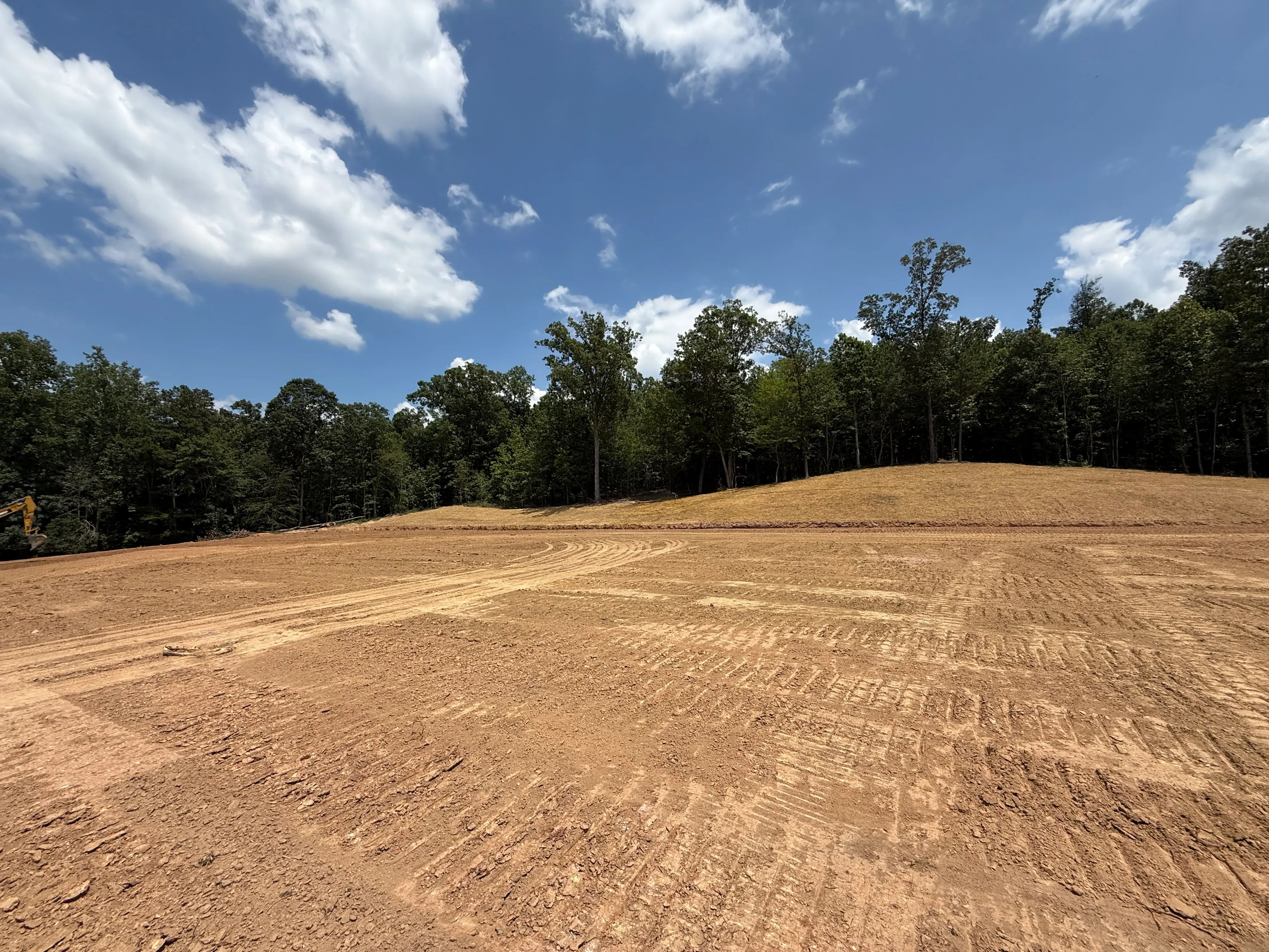 Cleared and graded dirt site with tree line, showing excavation and land preparation work