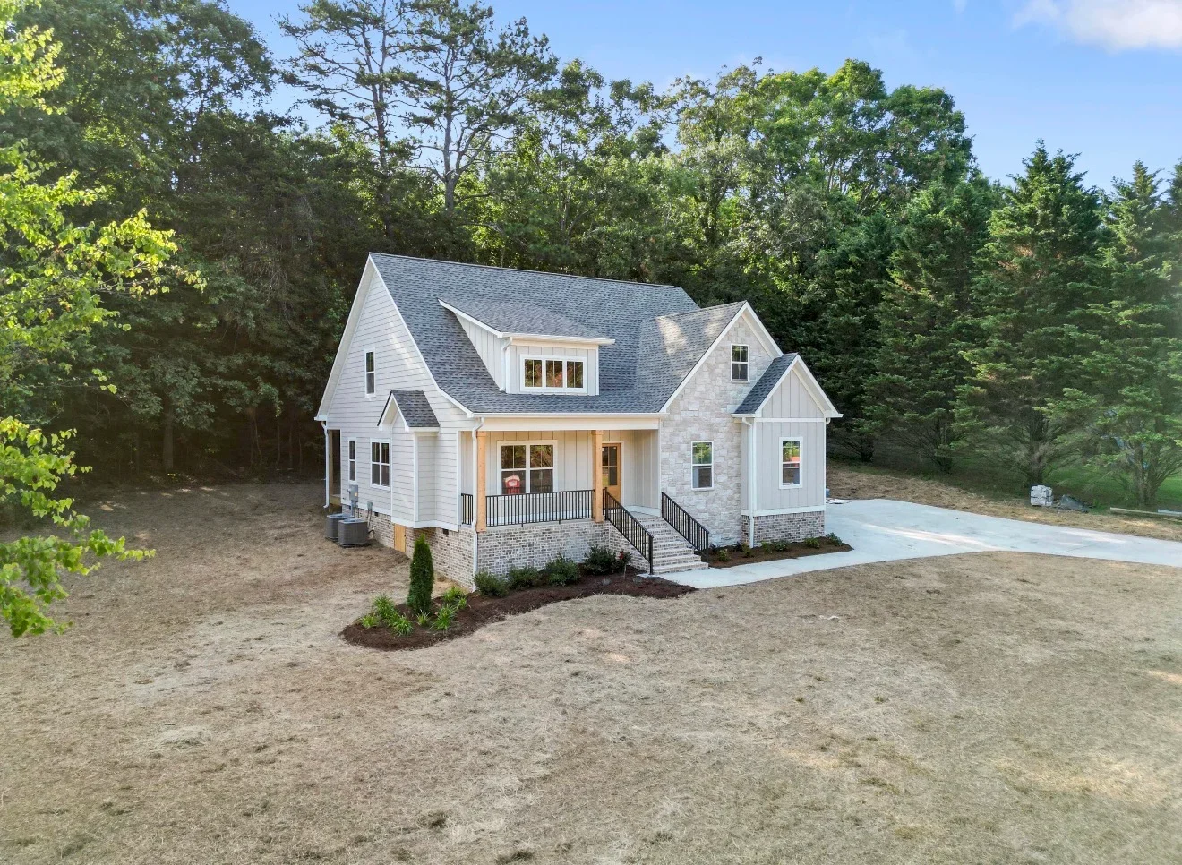 White farmhouse with brick foundation, metal porch railings, and concrete driveway