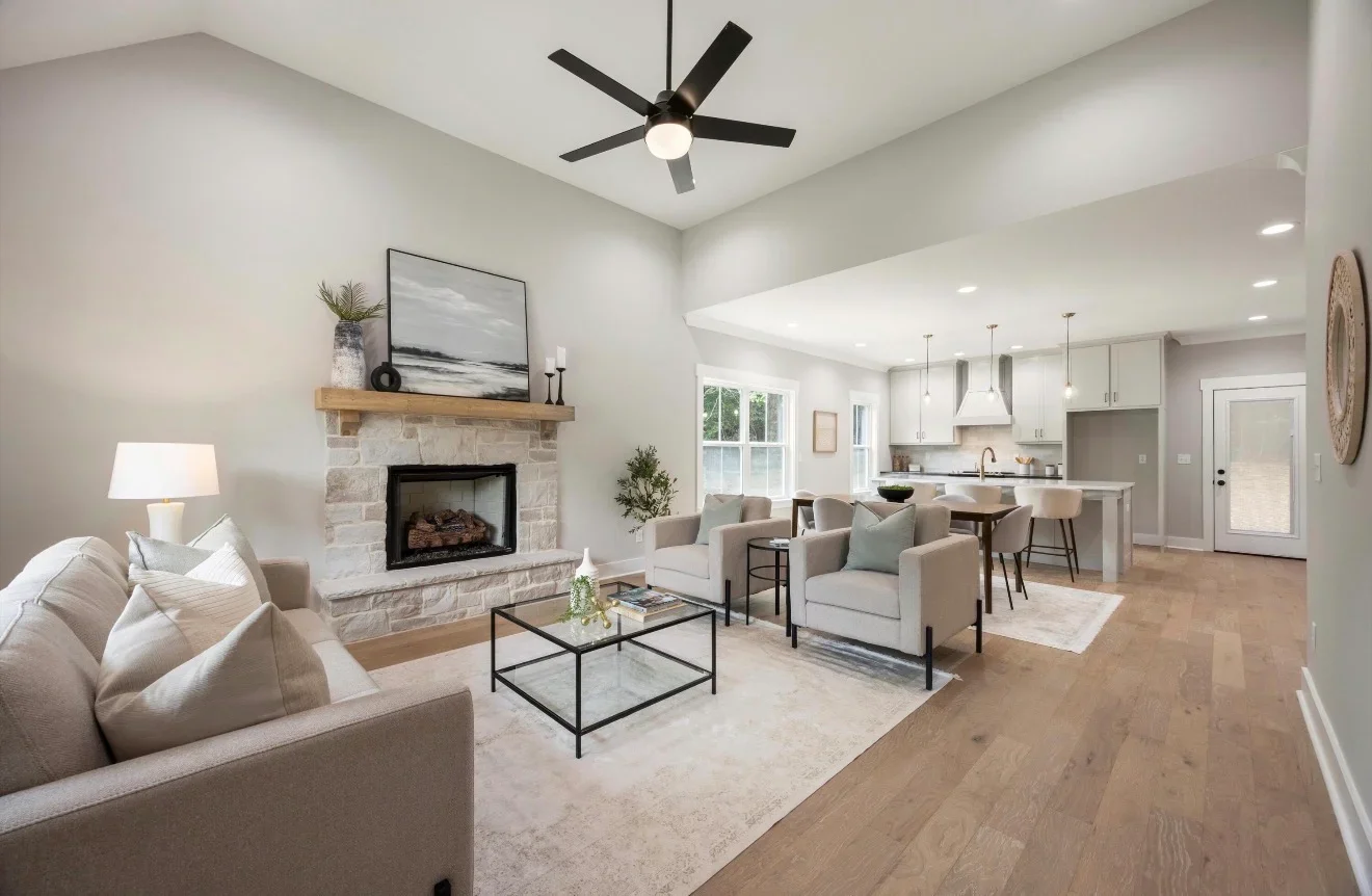 Open concept living room with stone fireplace, hardwood floors, white kitchen, and vaulted ceiling