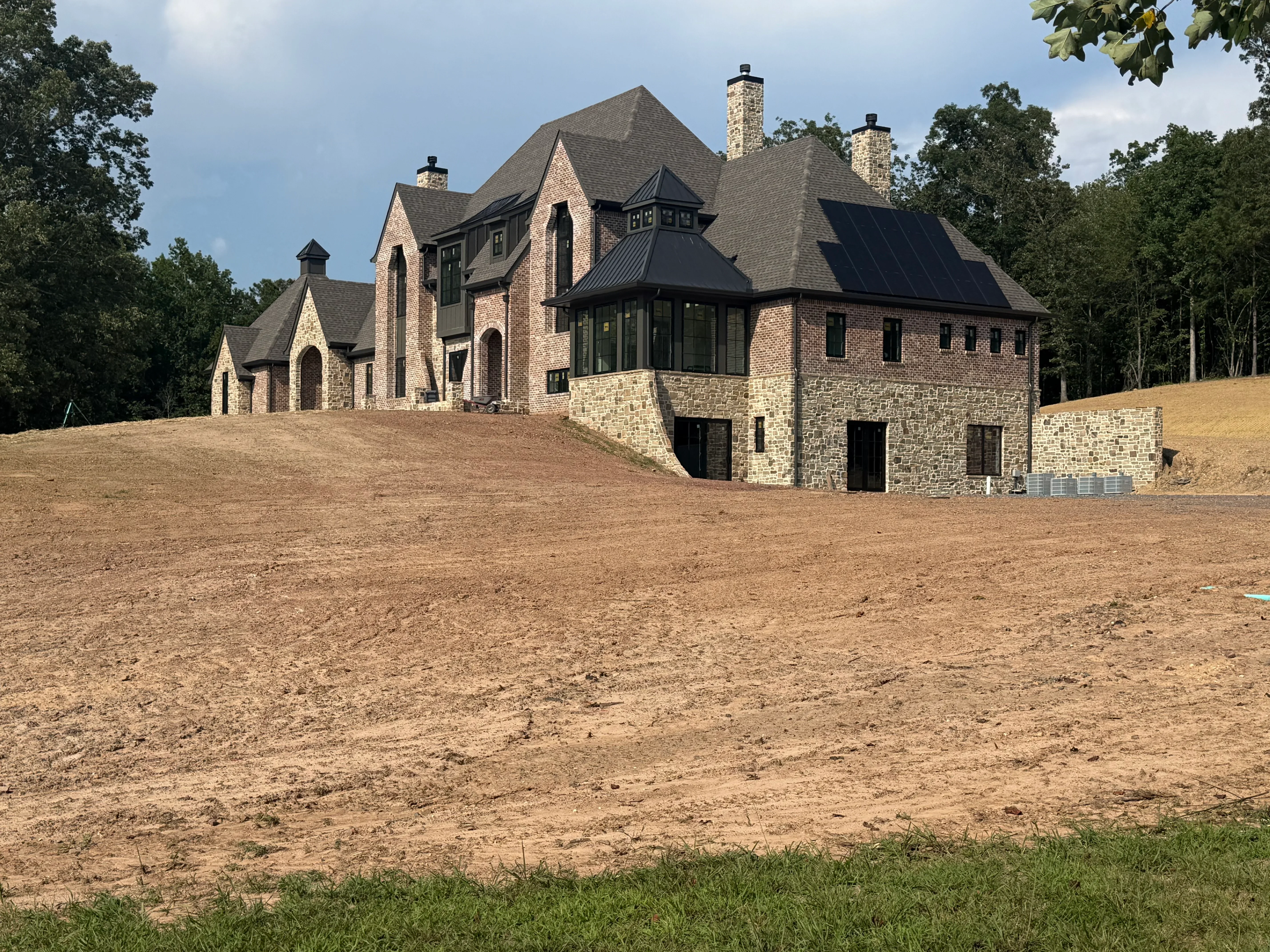 Multi-story brick and stone home with metal roof, gables, and stone veneer foundation during construction phase