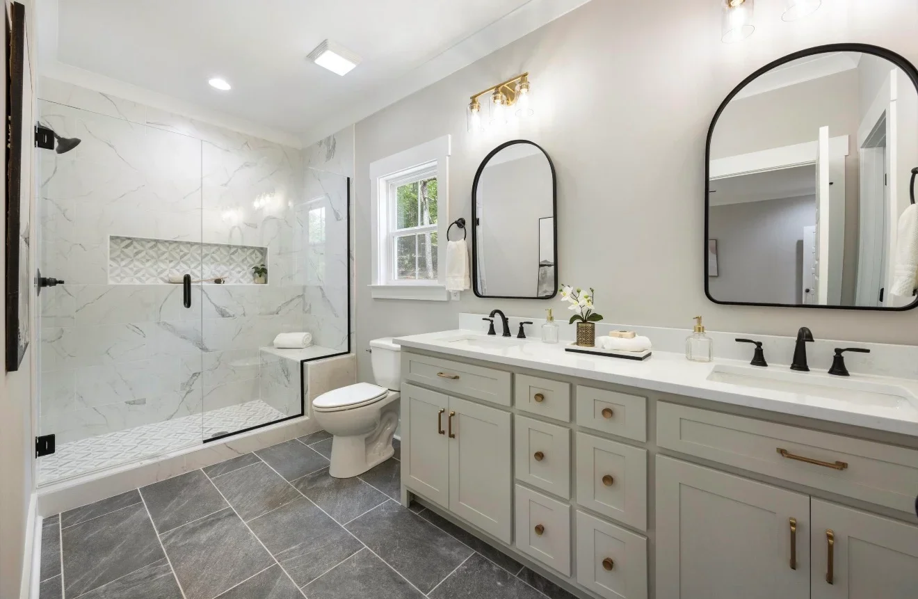 Marble tile bathroom with dual vanity, frameless glass shower, and black-framed mirrors