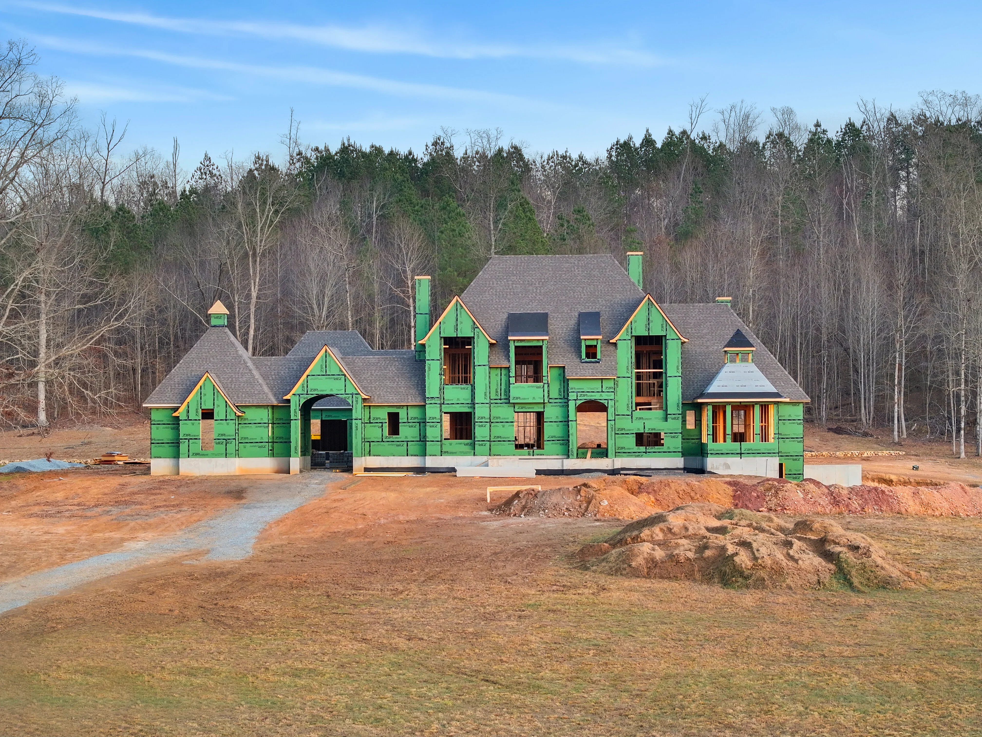 Green house wrap exterior sheathing on multi-gable home framing with gray roof and prepared openings
