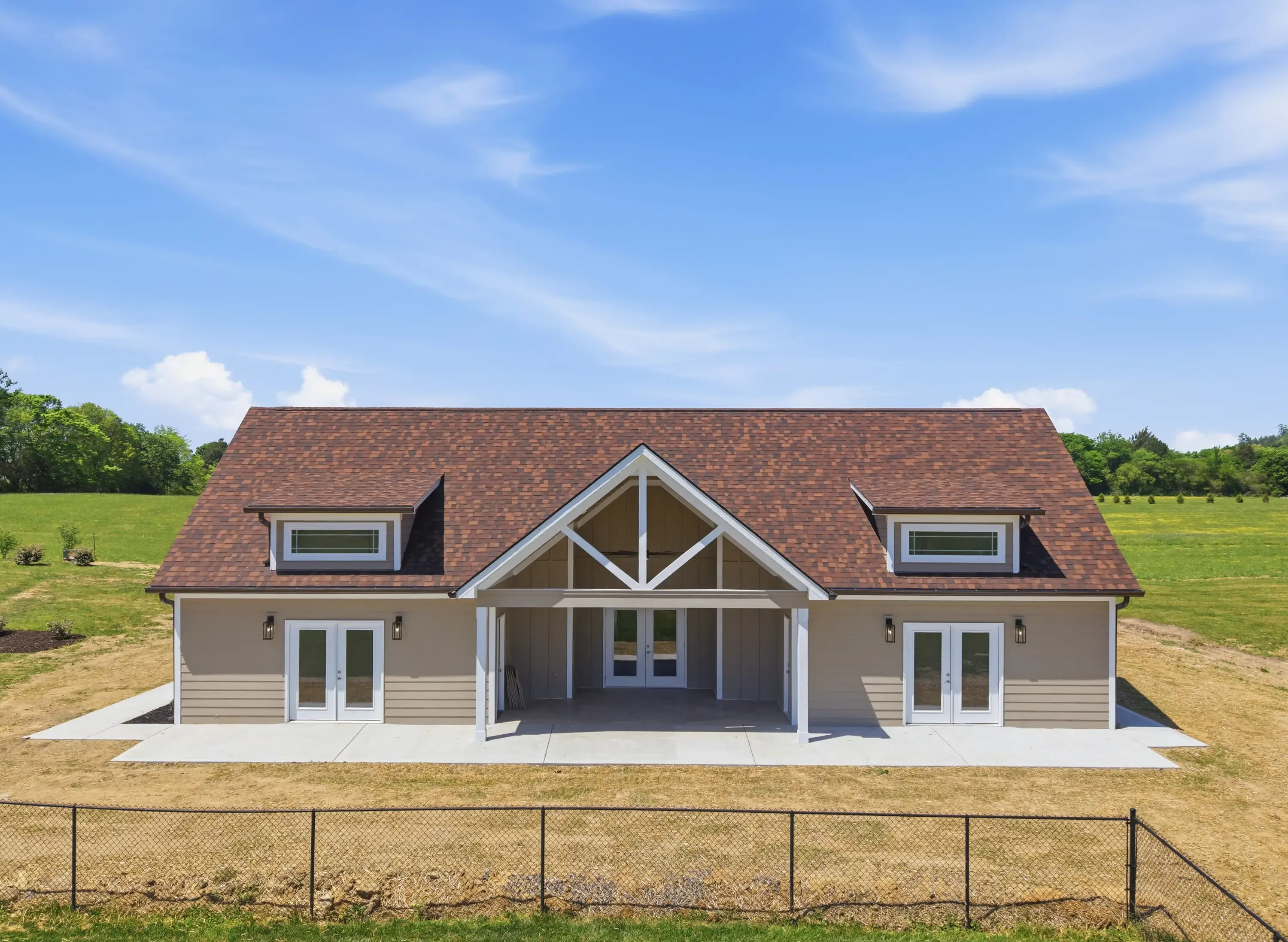 New home with brown shingle roof, tan siding, white trim, concrete patio, and covered entry portico