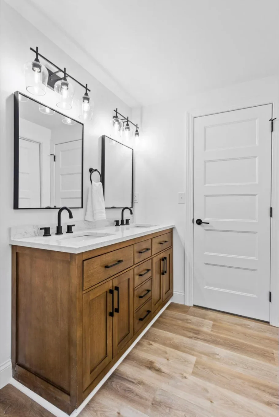 Dual-sink bathroom vanity with wood cabinets, quartz countertop, black mirrors and lighting fixtures